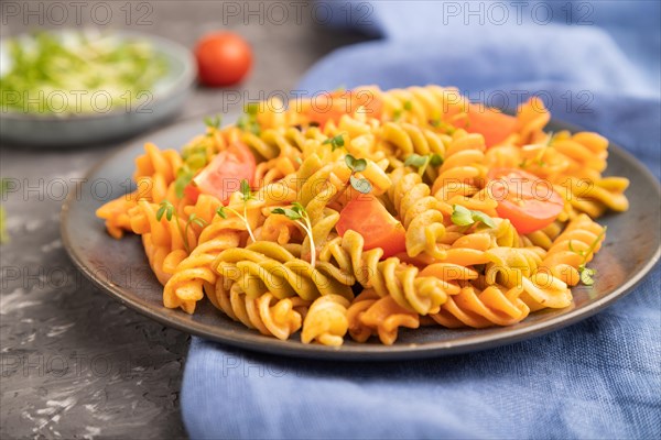 Tortiglioni semolina pasta with tomato and microgreen sprouts on a black concrete background and blue textile. Side view, close up, selective focus
