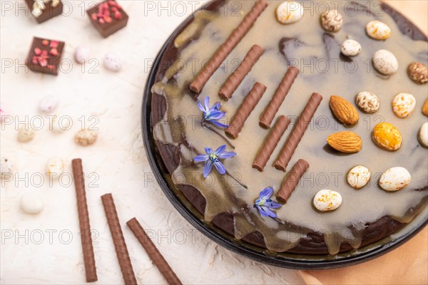 Homemade chocolate brownie cake with caramel cream and almonds with cup of coffee on a white concrete background and orange textile. Side view, close up, selective focus