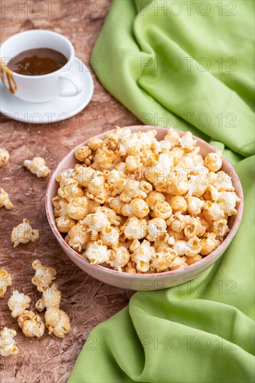 Popcorn with caramel in ceramic bowl on brown concrete background and green textile. Side view, close up