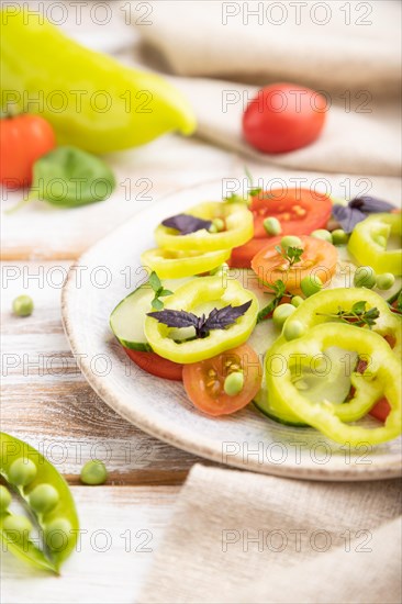 Vegetarian salad from green pea, tomatoes, pepper and basil on white wooden background and linen textile. Side view, close up, selective focus