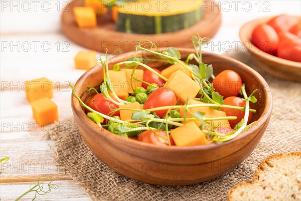 Vegetarian vegetable salad of tomatoes, pumpkin, microgreen pea sprouts on white wooden background and linen textile. Side view, close up, selective focus