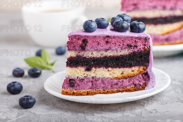 Homemade cake with souffle cream and blueberry jam with cup of coffee and fresh blueberries on a gray concrete background. side view, selective focus, close up