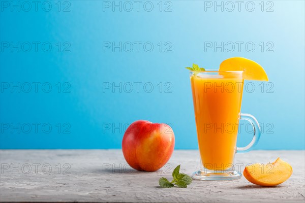 Glass of peach juice on a gray and blue background. Morninig, spring, healthy drink concept. Side view, copy space