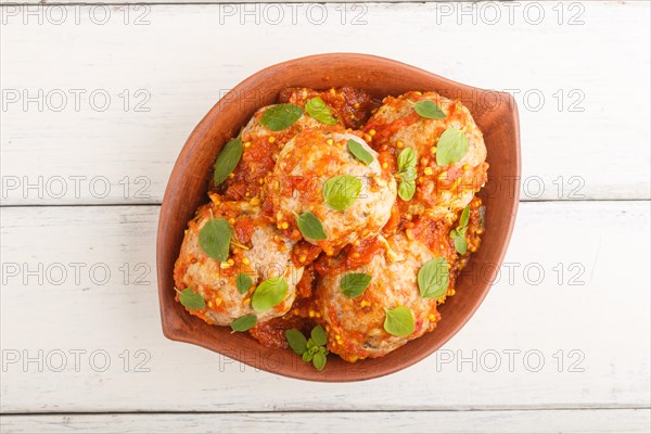 Pork meatballs with tomato sauce, oregano leaves, spices and herbs in clay bowl on a white wooden background. top view, flat lay, close up