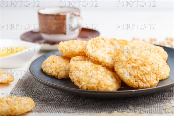 Traditional japanese rice chips cookies with honey and soy sauce on a blue ceramic plate and a cup of coffee on a white wooden background. side view, close up, selective focus
