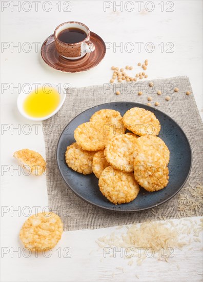 Traditional japanese rice chips cookies with honey and soy sauce on a blue ceramic plate and a cup of coffee on a white wooden background. side view, close up