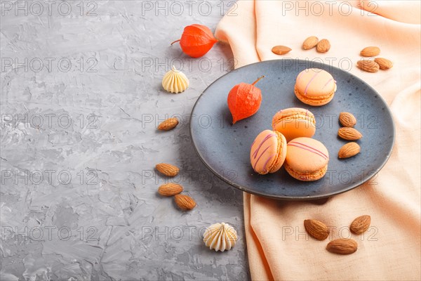 Orange macarons or macaroons cakes on blue ceramic plate on a gray concrete background and orange textile. side view, copy space