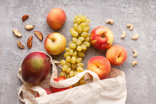 Fruits in reusable cotton textile white bag. Zero waste shopping, storage and recycling concept, eco friendly lifestyle. Top view, flat lay, close up. Peach, apple, nuts, mango, grape