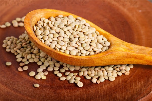 Pile of green lentils in a wooden spoon on brown background. Closeup