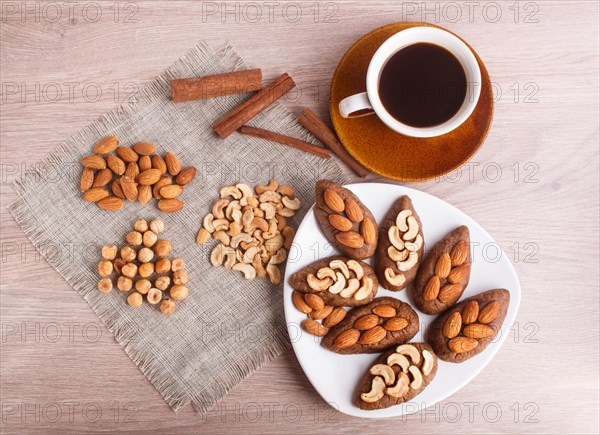 Small cakes potatoes with almonds and cashew nuts on a dessert plate. A cup of coffee, cinnamon, almonds, hazelnuts, cashew on a linen napkin. Still life. Copy space