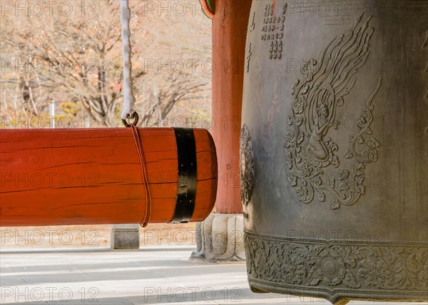 Large red wooden gong on linen wrapped chain hanging next to traditional metal Buddhist temple bell in South Korea
