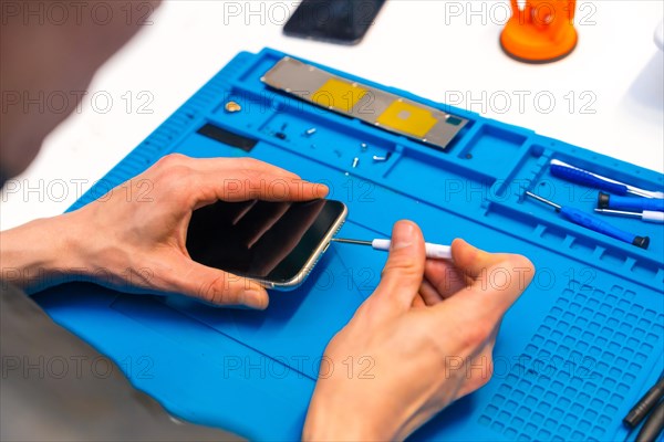 Close-up with elevated view of the hands of a man repairing a mobile phone in small workshop