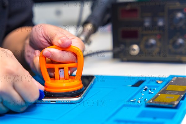 Close-up of a man using pick and suction cup to repair a mobile phone in a workshop