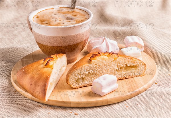 Sweet buns, meringues and coffee cup on a wooden board and linen tablecloth