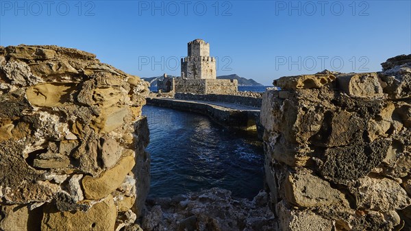 View through a crumbling bridge to a castle by the sea under a deep blue sky, octagonal medieval tower. Islet of Bourtzi, sea fortress of Methoni, Peloponnese, Greece, Europe