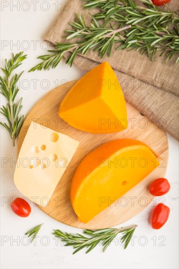Various types of cheese with rosemary and tomatoes on wooden board on a white wooden background and linen textile. Top view, close up, flat lay
