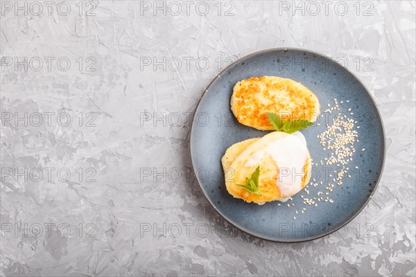 Cheese pancakes on a blue ceramic plate with milk sauce on a gray concrete background. top view, flat lay, copy space