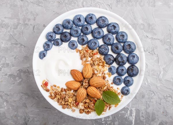 Yoghurt with blueberry, granola and almond in white plate on gray concrete background. top view, flat lay, close up