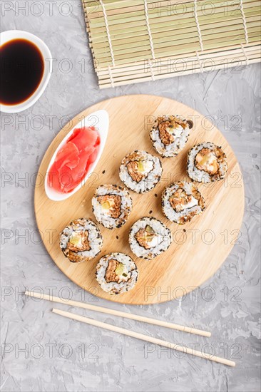 Japanese maki sushi rolls with salmon, sesame, cucumber chopsticks, soy sauce and marinated ginger on wooden board on a gray concrete background. Top view, flat lay
