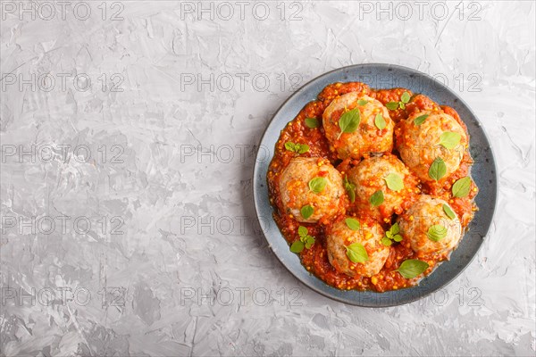 Pork meatballs with tomato sauce, oregano leaves, spices and herbs on blue ceramic plate on a gray concrete background. top view, flat lay, copy space