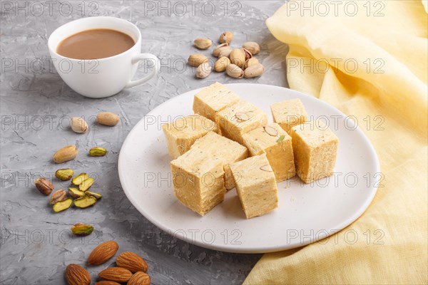 Traditional indian candy soan papdi in white plate with almond, pistache and a cup of coffee on a gray concrete background with yellow textile. side view, close up