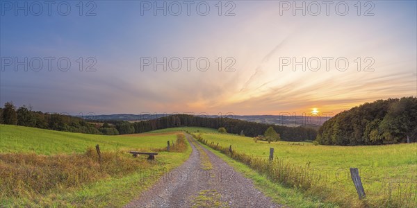 A small bench stands at the edge of a path with a view of the Weserbergland, landscape format, panorama, landscape shot, nature shot, sunset, evening mood, Goldbeck, Rinteln, Lower Saxony, Germany, Europe