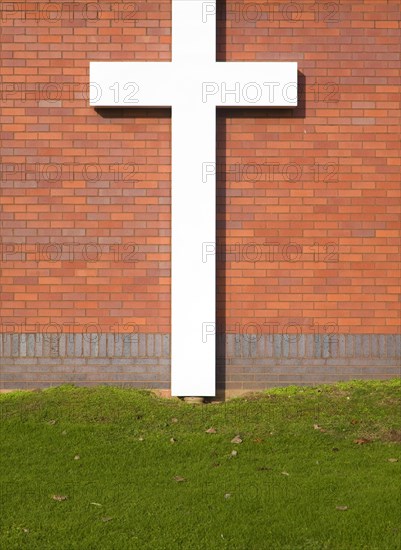 Large white crucifix cross against brick wall on grass lawn River of Life Church, Felixstowe, Suffolk, England, United Kingdom, Europe