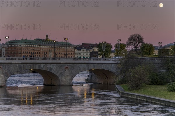 Evening view of a city with a bridge over a river and the moon in the twilight sky Stockholm