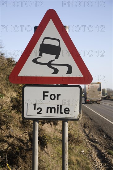 Red triangular road sign warning of slippery road surface ahead for half a mile, UK