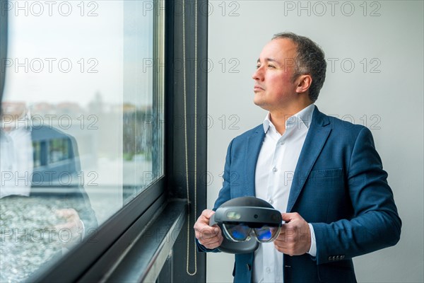 Businessman looking through the window with futuristic virtual reality goggles focusing on the successful future