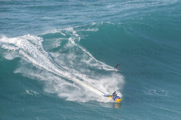A surfer rides a high wave and is accompanied by a jet ski, Nazare, Portugal, Europe