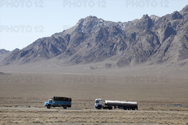 An old round-hood Mercedes truck in front of a new Mercedes truck on a motorway in the central desert of Iran, 13.03.2019