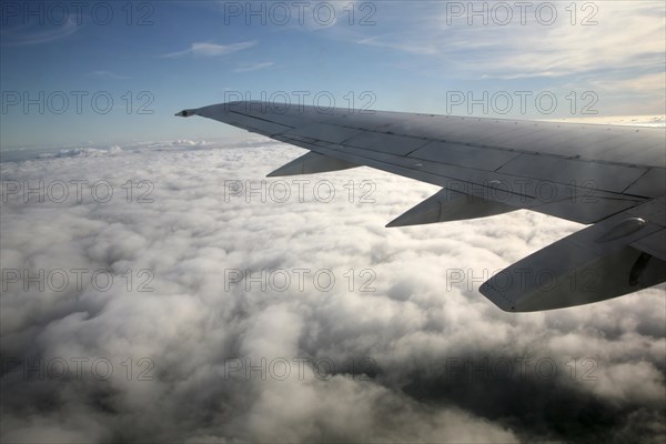 Aeroplane wing of plane cruising in blue sky high above clouds over Europe