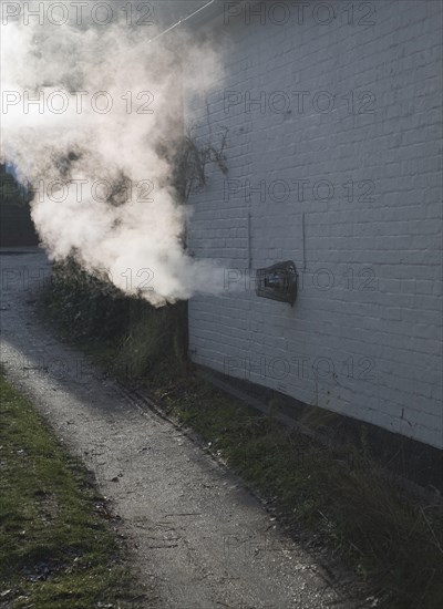 Heat steam emissions from domestic oil powered boiler heating system released through wall of house into the air