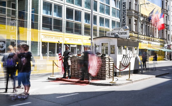 A long exposure shows a tourist at Checkpoint Charlie, men in American military uniforms stand in the guardhouse, Berlin 04.05.2018