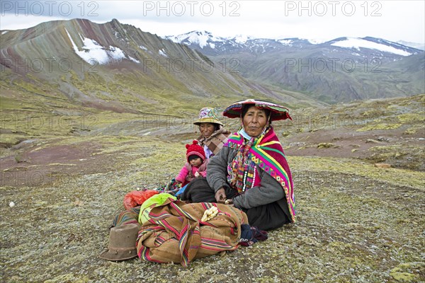 Peruvian woman, 55 and 27 years old, in traditional dress sit with a toddler, 7 months, in a field eating potatoes, in the background the Cordillera de Colores or Rainbow Mountains in Palccoyo, Checacupe district, Canchis province, Cusco region, Peru, South America