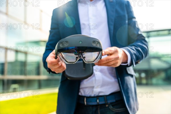 Cropped photo with close-up of the hands of a businessman holding a innovative augmented vision glasses outdoors