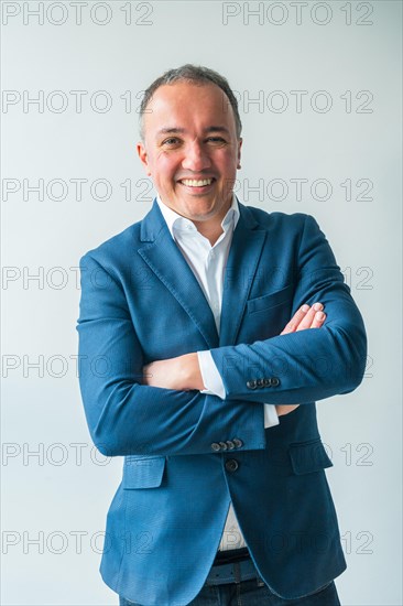 Vertical three quarter length studio portrait of a confident businessman standing proud with arms crossed and smiling at camera