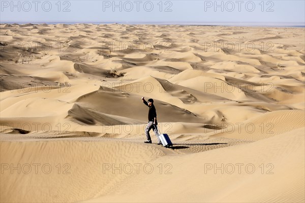 Symbolic image, tourist with suitcase in the desert, Mesr Desert, Iran. The Mesr Desert is part of the central Dashte-Kavir desert, 12.03.2019