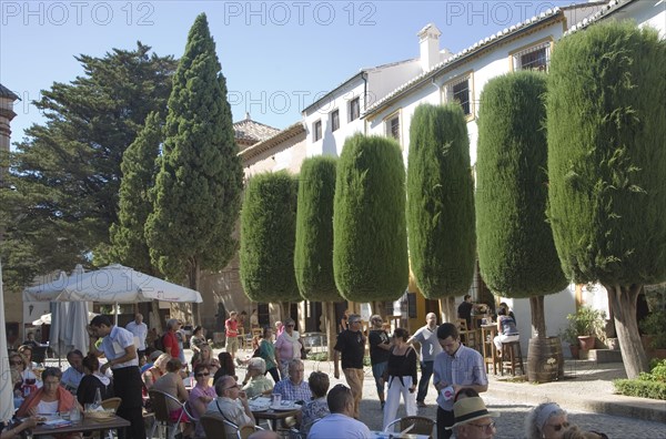 Groups of people sitting at tables and chairs of outdoor street cafe in the old city of Ronda, Spain, Europe