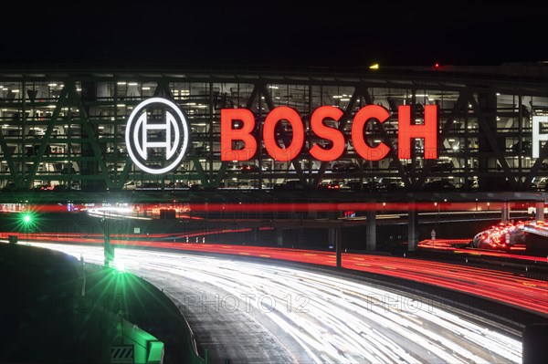 A8 motorway at Stuttgart Airport with Bosch multi-storey car park in the evening, cars create light trails. The 440 metre long construction offers space for 4200 vehicles. Bosch owns the naming rights, the stylised ignition anchor measures 12 metres in diameter. This makes it one of the largest neon signs in the world. Stuttgart, Baden-Wuerttemberg, Germany, Europe