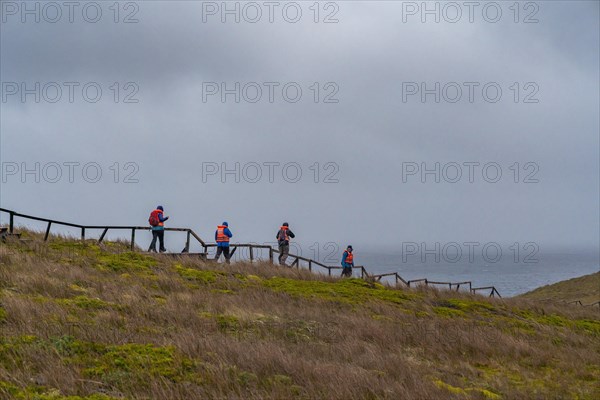 Passengers of the cruise ship Stella Australis in life jackets hike in storm and rain to Cape Horn, southernmost point of America, Horn Island, Cabo de Hornos National Park, Tierra del Fuego, Patagonia, Chile, South America