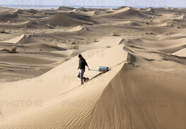 Symbolic image, tourist with suitcase in the desert, Mesr Desert, Iran. The Mesr Desert is part of the central Dashte-Kavir desert, 12.03.2019