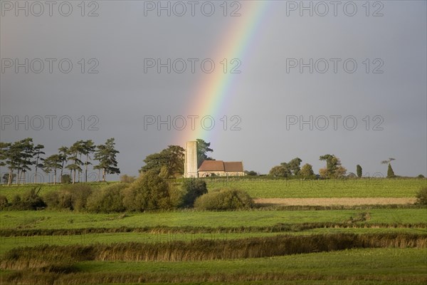 The end of a rainbow lights up the tower of All Saints church, Ramsholt, Suffolk, England, United Kingdom, Europe