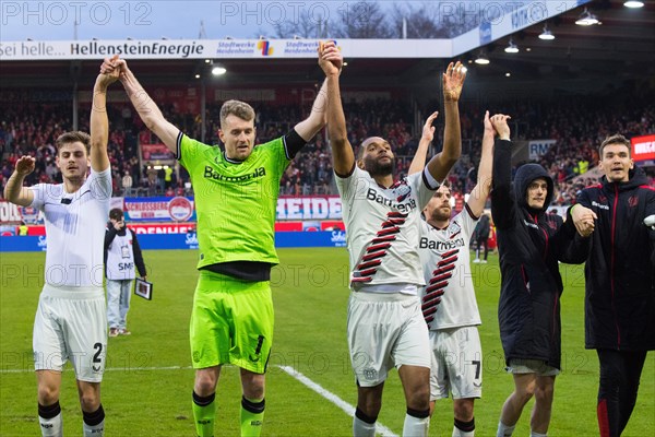 Football match, the Bayer Leverkusen players from left to right: Josip STANISIC, goalkeeper and captain Lukas HRADECKY, Jonathan TAH, Jonas HOFMAN hidden, Florian WIRTZ and Patrik SCHICK celebrate the victory with their travelling fans in the fan curve, Voith-Arena football stadium, Heidenheim