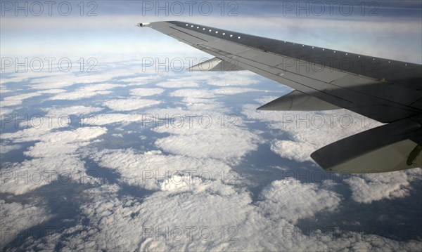 Aeroplane wing of plane cruising in blue sky high above clouds over Europe