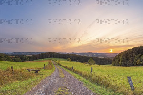 A small bench stands at the edge of the path with a view of the Weserbergland, landscape format, landscape shot, nature shot, sunset, evening mood, Goldbeck, Rinteln, Lower Saxony, Germany, Europe