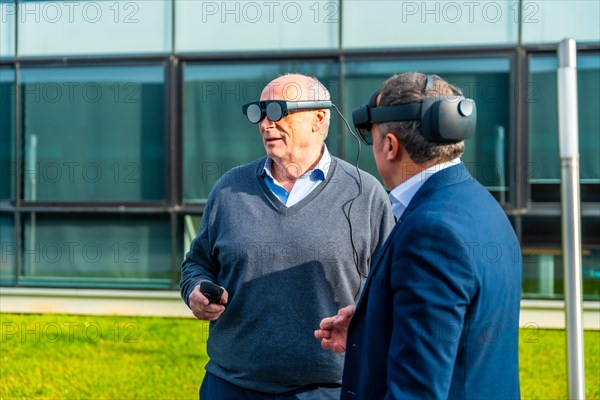 Two aged businessmen partners testing virtual reality headset outdoors in a sunny day