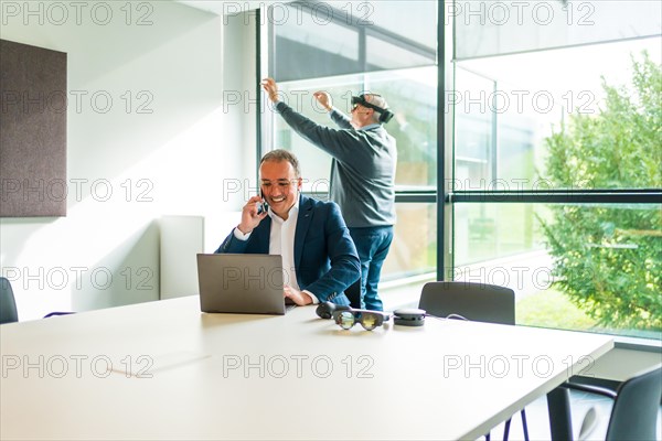 Businessman working using laptop while a colleague is using VR googles in the office