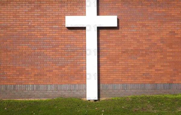 Large white crucifix cross against brick wall on grass lawn River of Life Church, Felixstowe, Suffolk, England, United Kingdom, Europe